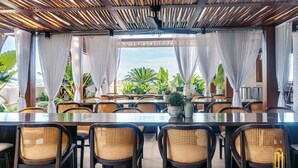 A restaurant with a long table and wicker chairs, a ceiling fan, and a view of greenery outside. - Azzurro Hotel (Angeles City)