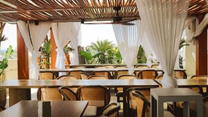 An outdoor restaurant with wooden tables and wicker chairs, draped with white curtains, and surrounded by greenery. - Azzurro Hotel (Angeles City)