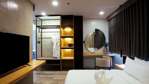 A modern hotel room with a large bed, a TV, a wooden desk, a mirror, and a robe rack. - Azzurro Hotel (Angeles City)