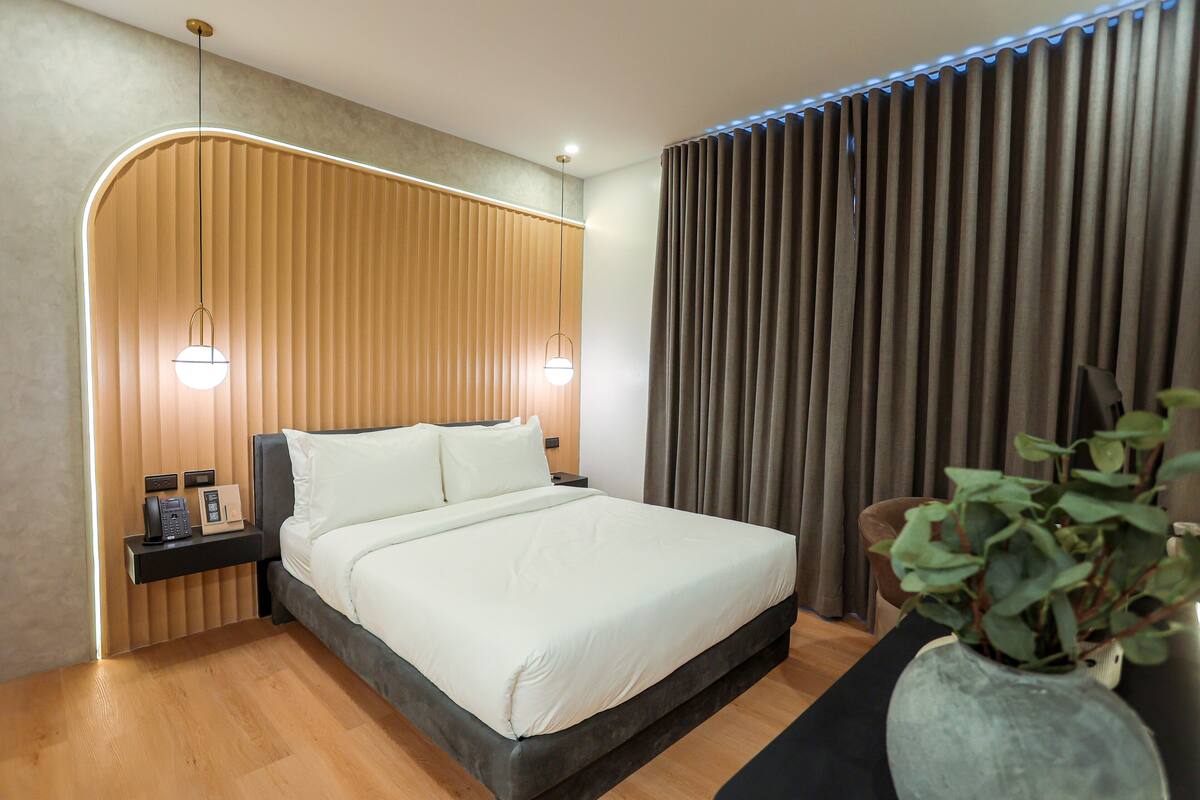 Un dormitorio moderno con una cama grande, pared de paneles de madera, lámparas de noche y una planta en maceta.