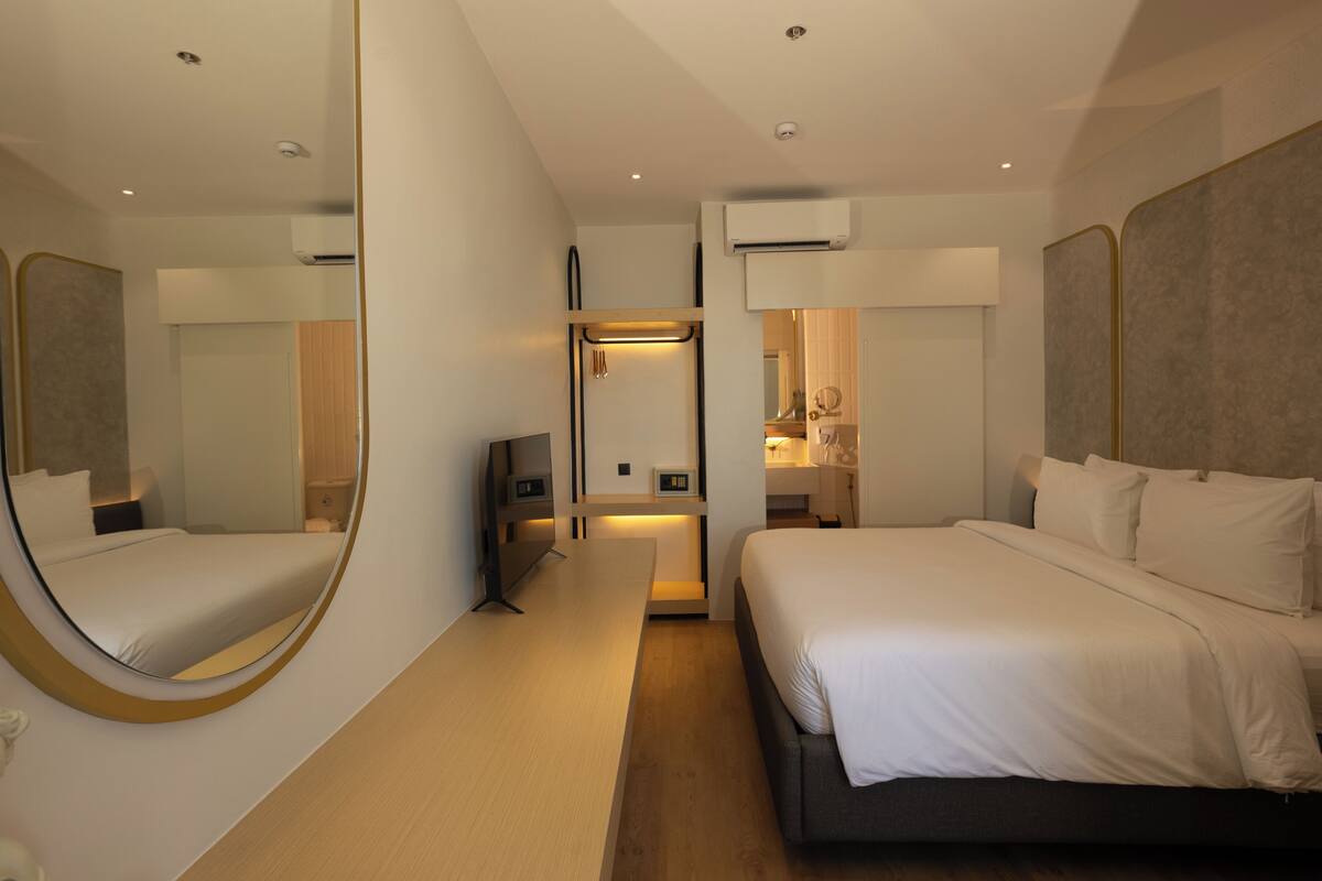 Una habitación de hotel moderna con una cama grande, una mesita de noche, un espejo y un armario.