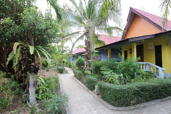 A pathway leading to a building with a red roof and yellow walls, surrounded by lush greenery and palm trees. - Lanta Villa Resort (Ko Lanta)