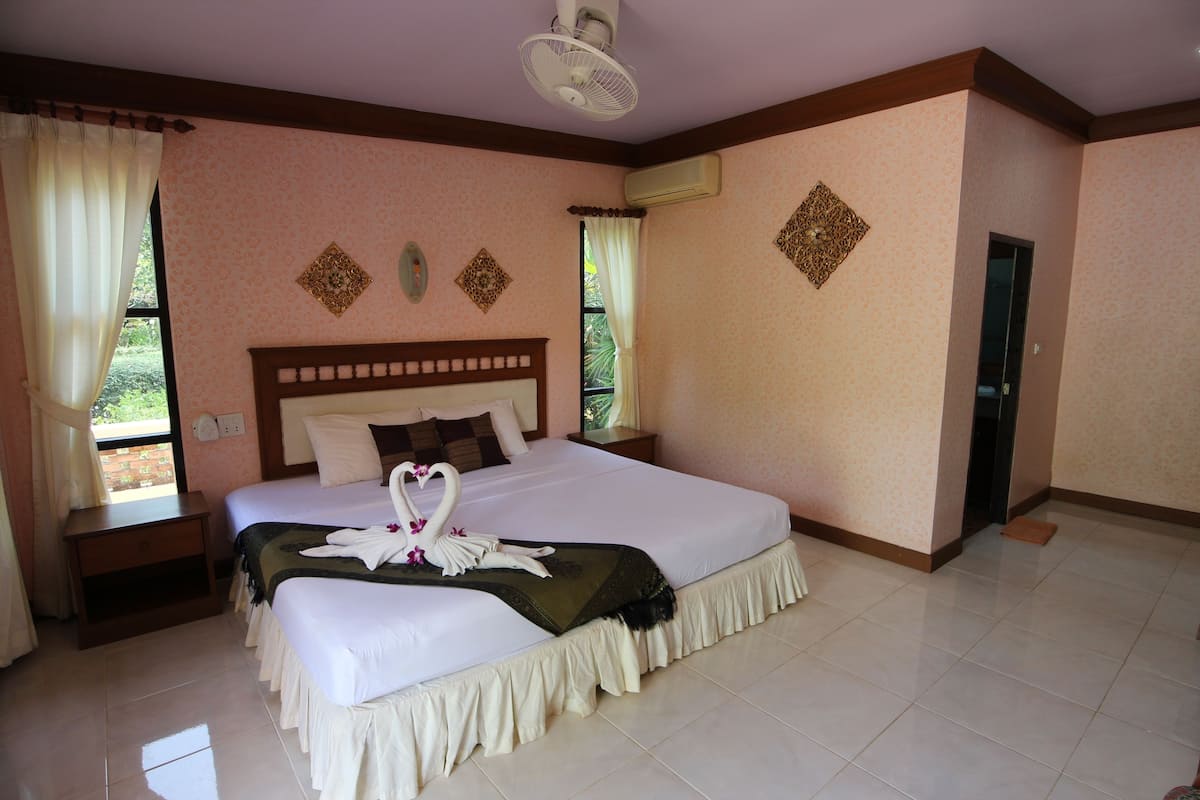 A spacious bedroom with a large bed, a nightstand, a bedside table, and a window with curtains.