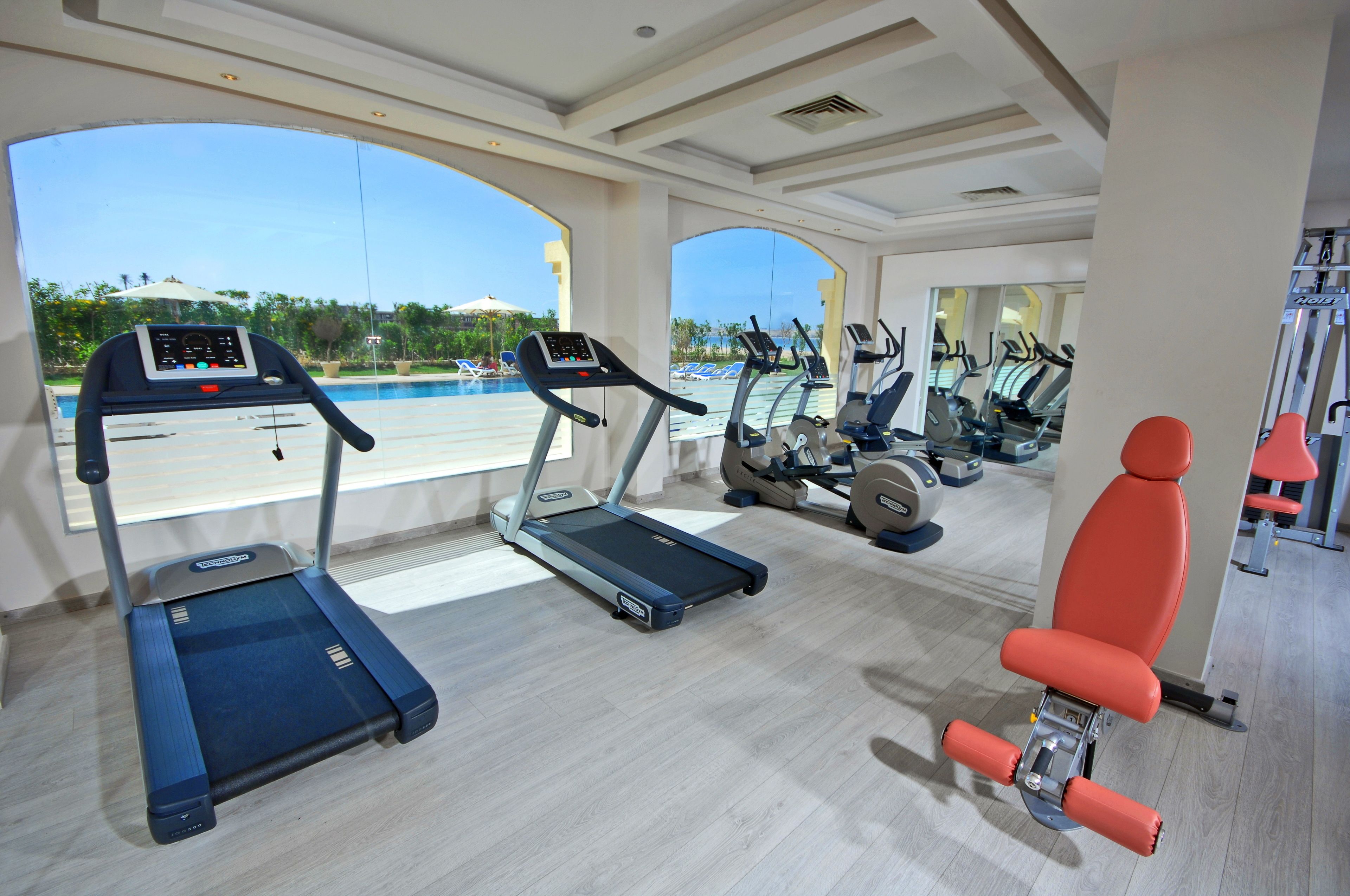 A gym with treadmills, exercise bikes, and a rowing machine, overlooking a pool area.