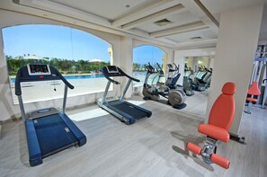 A gym with treadmills, exercise bikes, and a rowing machine, overlooking a pool area. - Tropitel Sahl Hasheesh Resort (Sahl Hasheeh)