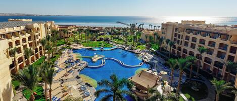 A resort with a large central pool, multiple balconies, and a view of the sea.
