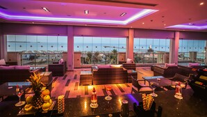 Un salón en la azotea con mobiliario de mimbre, una zona de bar y vistas a la ciudad.