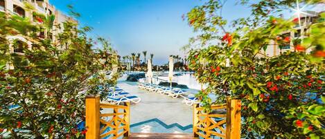 L’entrée d’un hôtel avec un portail en bois, un espace piscine avec des chaises longues et un ciel d’un bleu limpide.