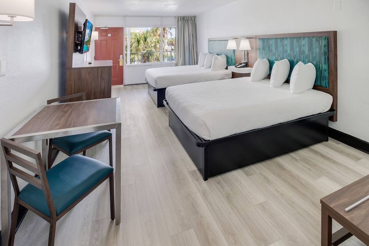 A hotel room with two beds, a desk, a chair, and a TV.