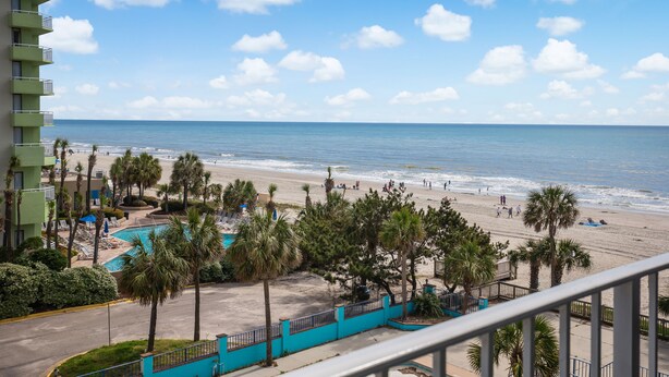 A beachfront hotel with a pool, palm trees, and a view of the ocean.