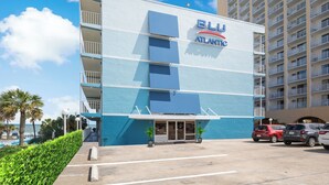 A hotel with a blue and white facade, balconies, and a parking lot with cars.