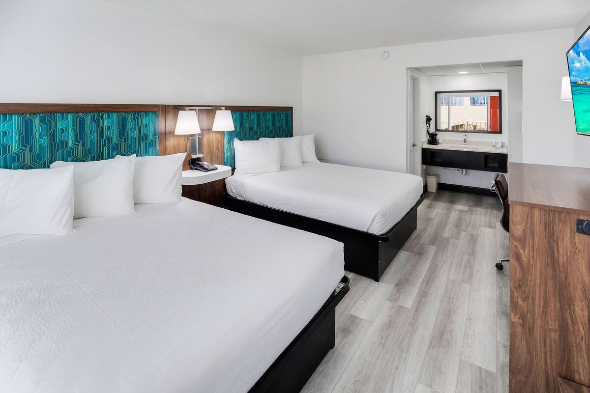 A hotel room with two beds, a small desk, a mirror, and a TV.