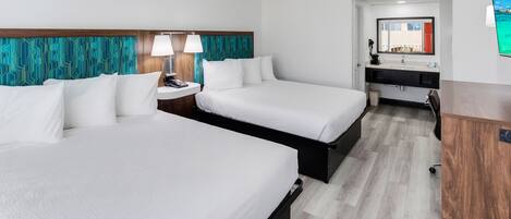 Una habitación de hotel con dos camas, un escritorio pequeño, un espejo y un televisor.
