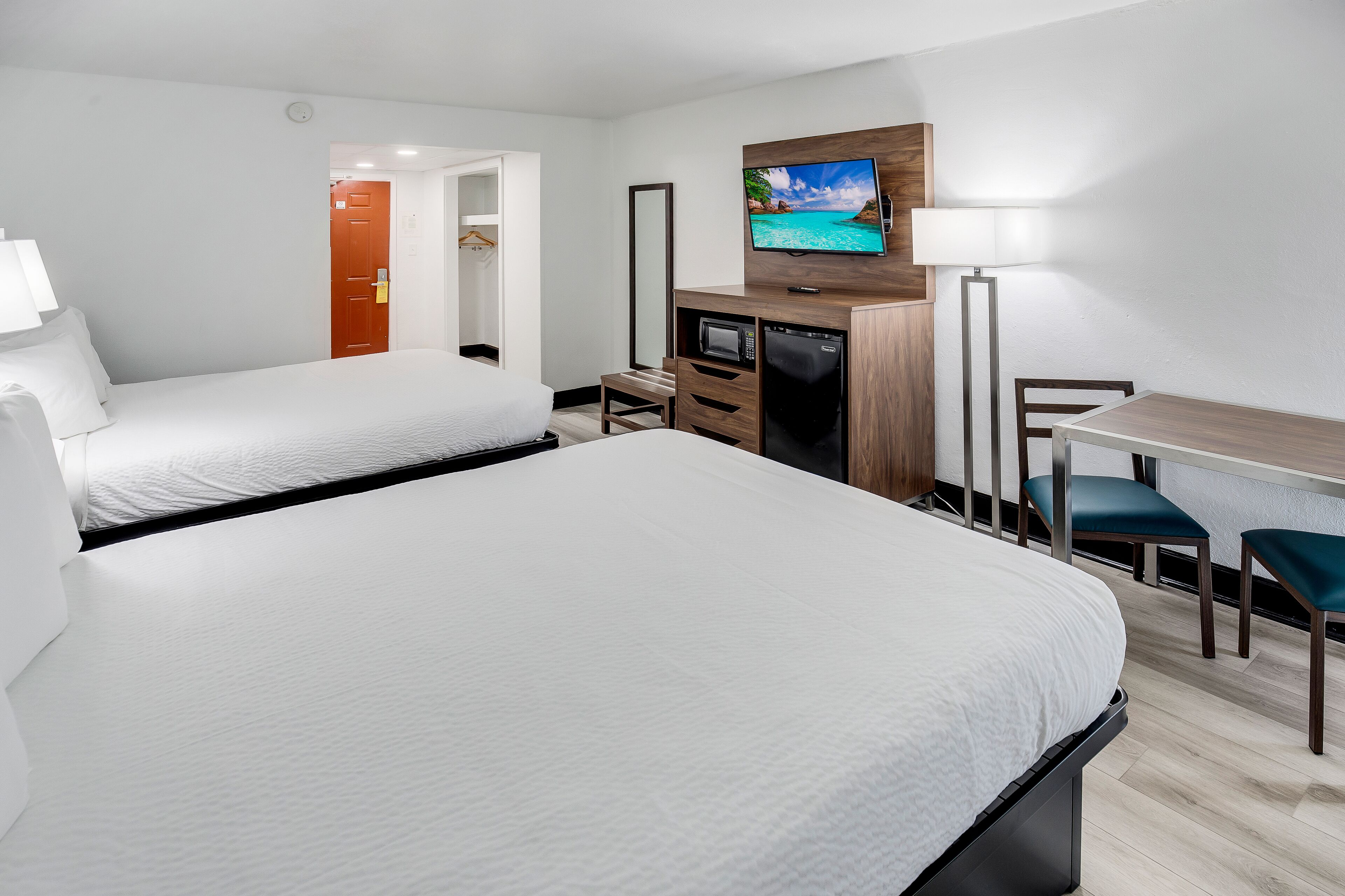 Une chambre d’hôtel avec deux lits, un bureau, une télévision, une lampe et une armoire.