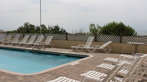 A pool area with white lounge chairs and a brick deck.