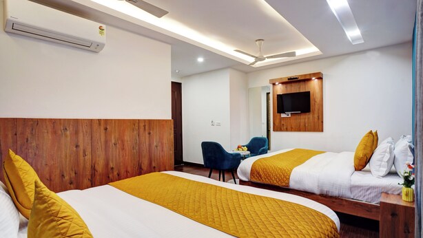 Ein Hotelzimmer mit zwei Betten, einem Holzkopfteil, einem Deckenventilator, einem an der Wand befestigten Fernseher und einem kleinen Tisch mit einem Stuhl.