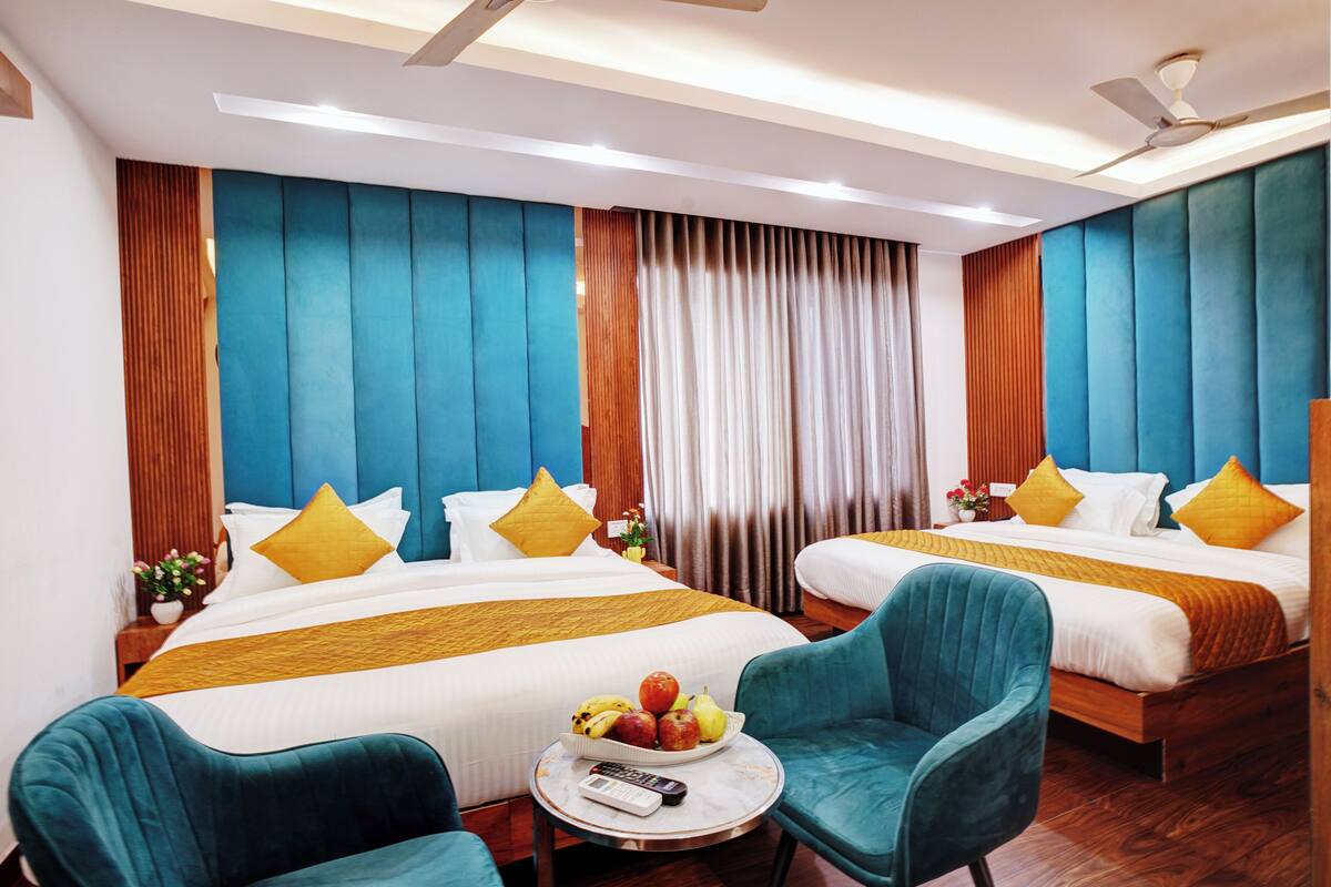 Ein Hotelzimmer mit zwei Betten, einem runden Tisch mit Obstschale und türkisfarbenen Sesseln.