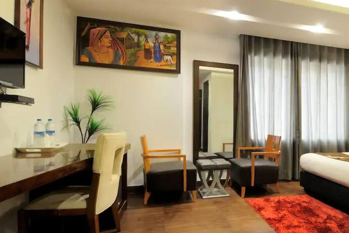 Ein Hotelzimmer mit Bett, Schreibtisch, Stuhl, kleinem Tisch, Spiegel und einem Gemälde an der Wand.