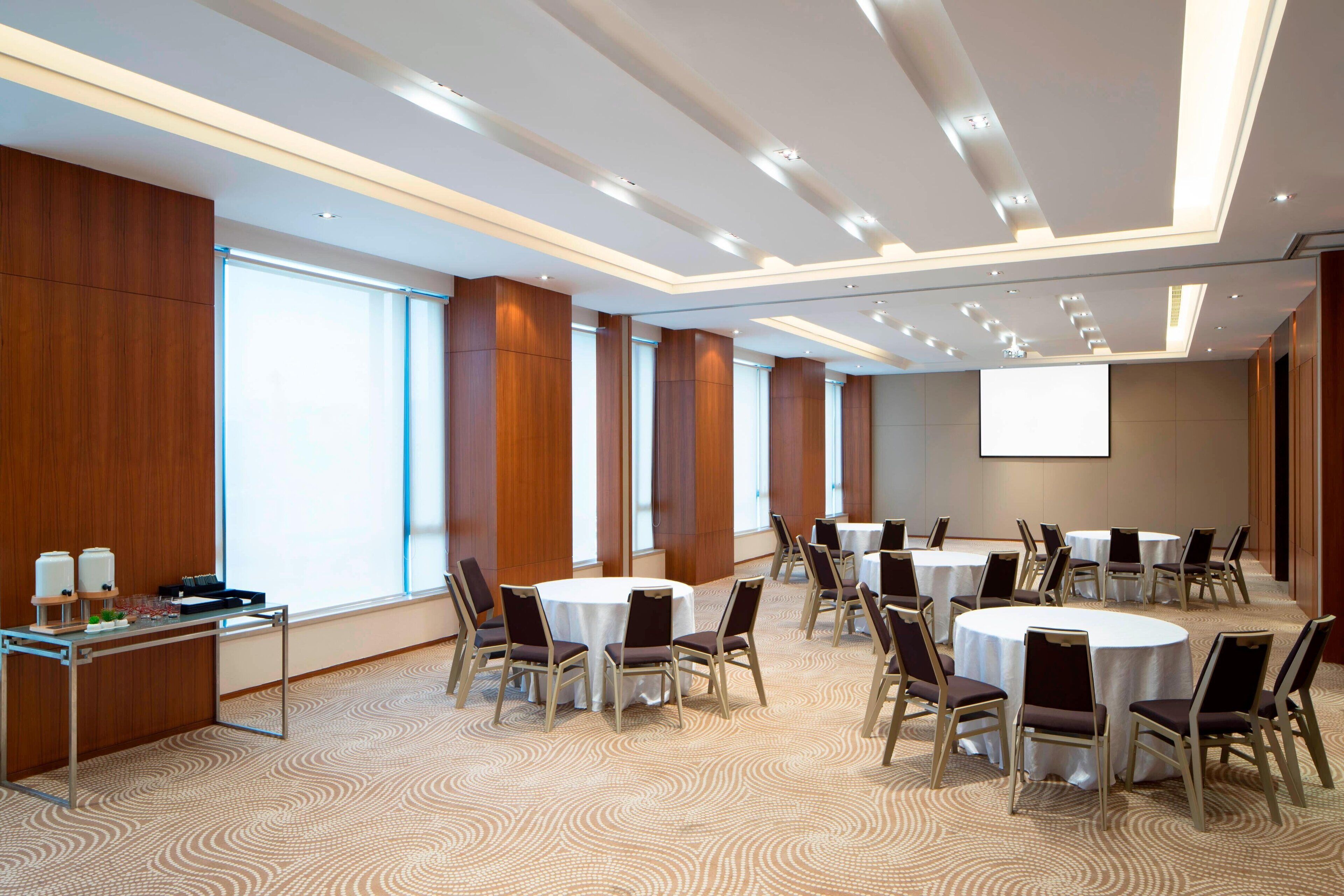 A conference room with round tables, chairs, a projection screen, and a presentation area.