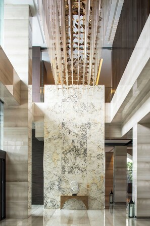 A modern lobby with a marble column, a wooden slatted ceiling, and a minimalist design.
