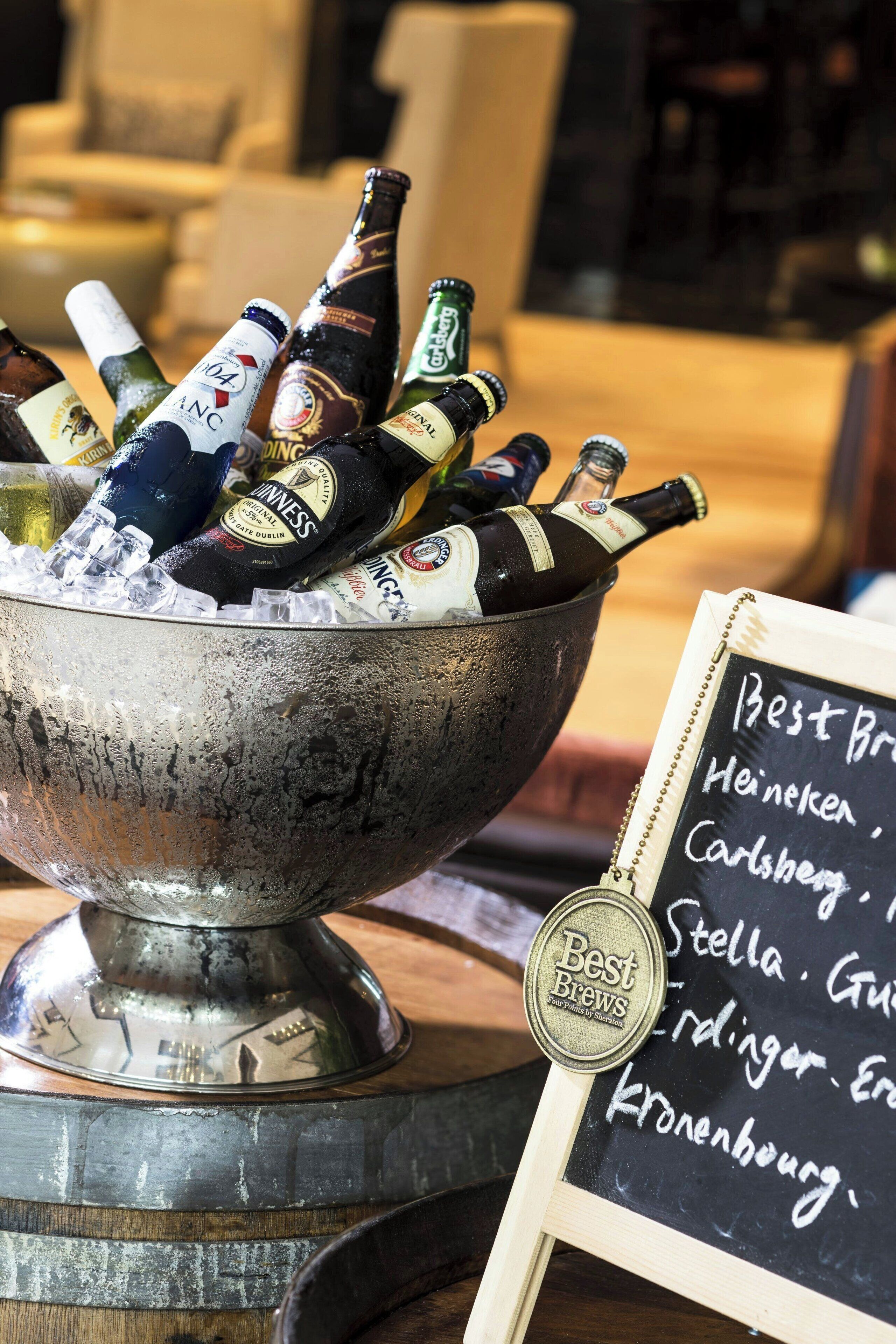 Un saladier en métal rempli de différentes bouteilles de bière, un tableau noir sur lequel figure une liste des types de bière, et un dessous de verre avec l’inscription « Les meilleures bières ».