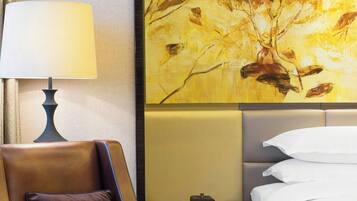 Ein Hotelzimmer mit braunem Ledersessel, einem Nachttisch mit Lampe, einem Bett mit weißer Bettwäsche und einem großen, abstrakten Gemälde an der Wand.