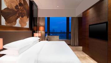 A hotel room with a large bed, a TV, a city view, and a modern design.