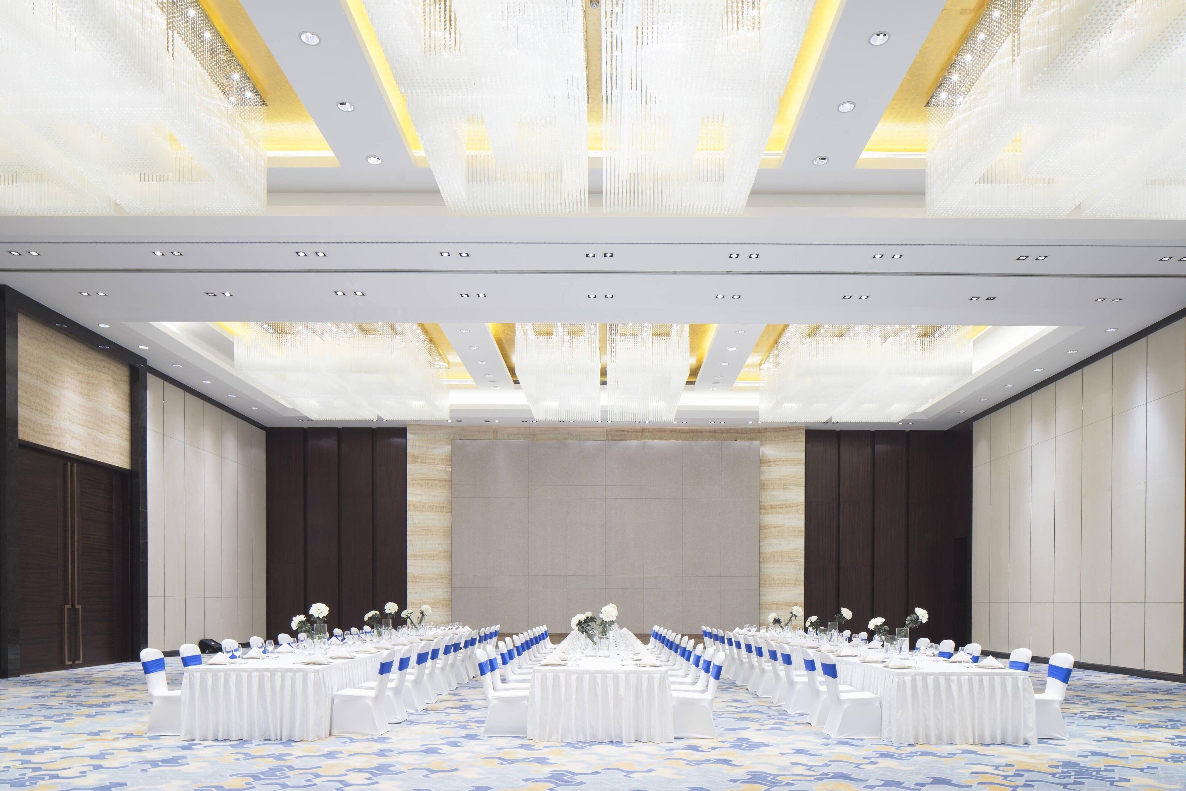 A banquet hall with round tables set for events, featuring white tablecloths and blue chair sashes.