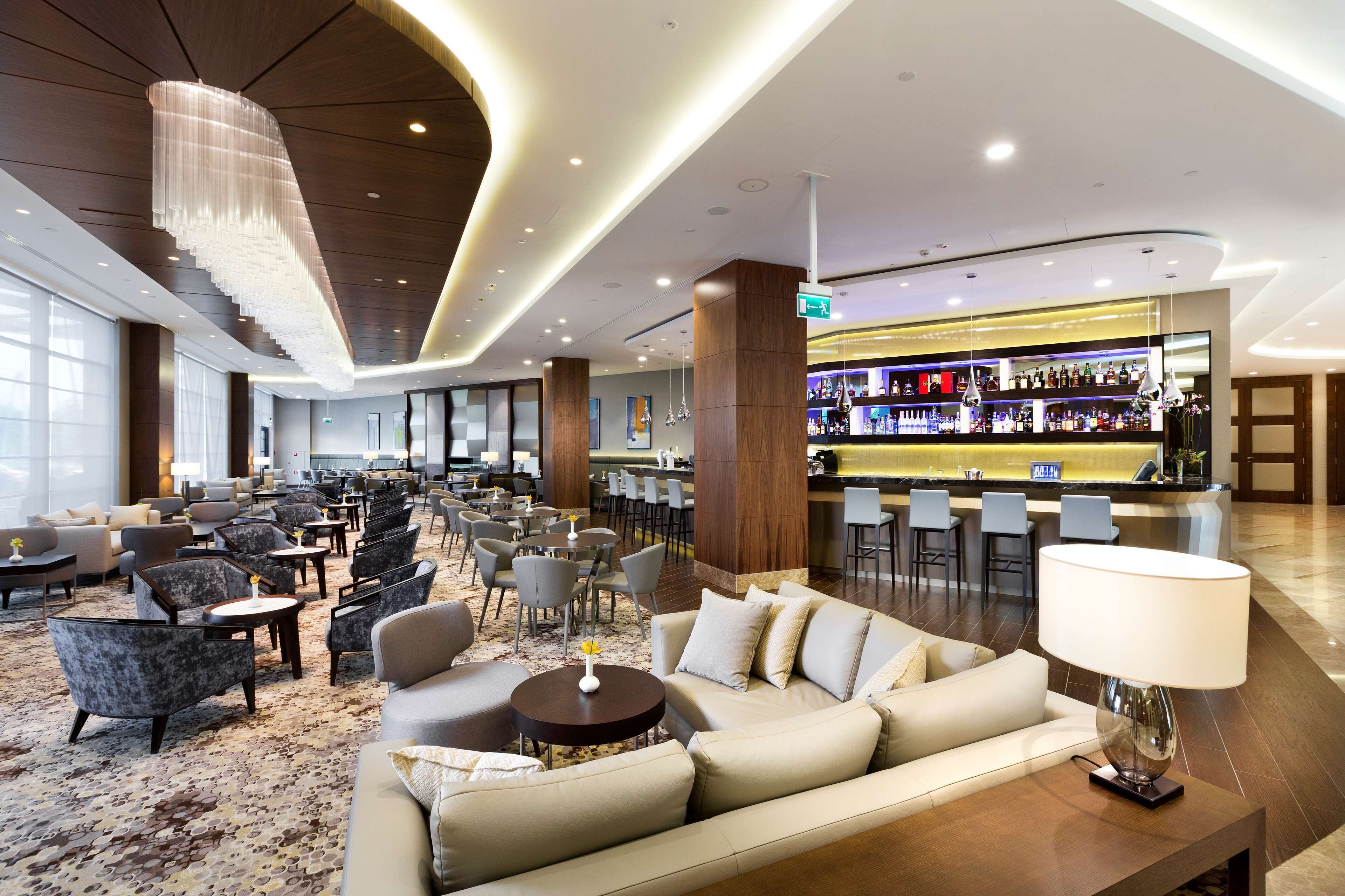 A spacious lobby with a bar area, seating arrangements, and a modern chandelier.