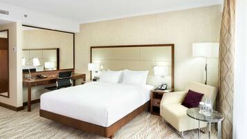 A hotel room with a large bed, a desk, a chair, a small table with bottles, and a mirror.