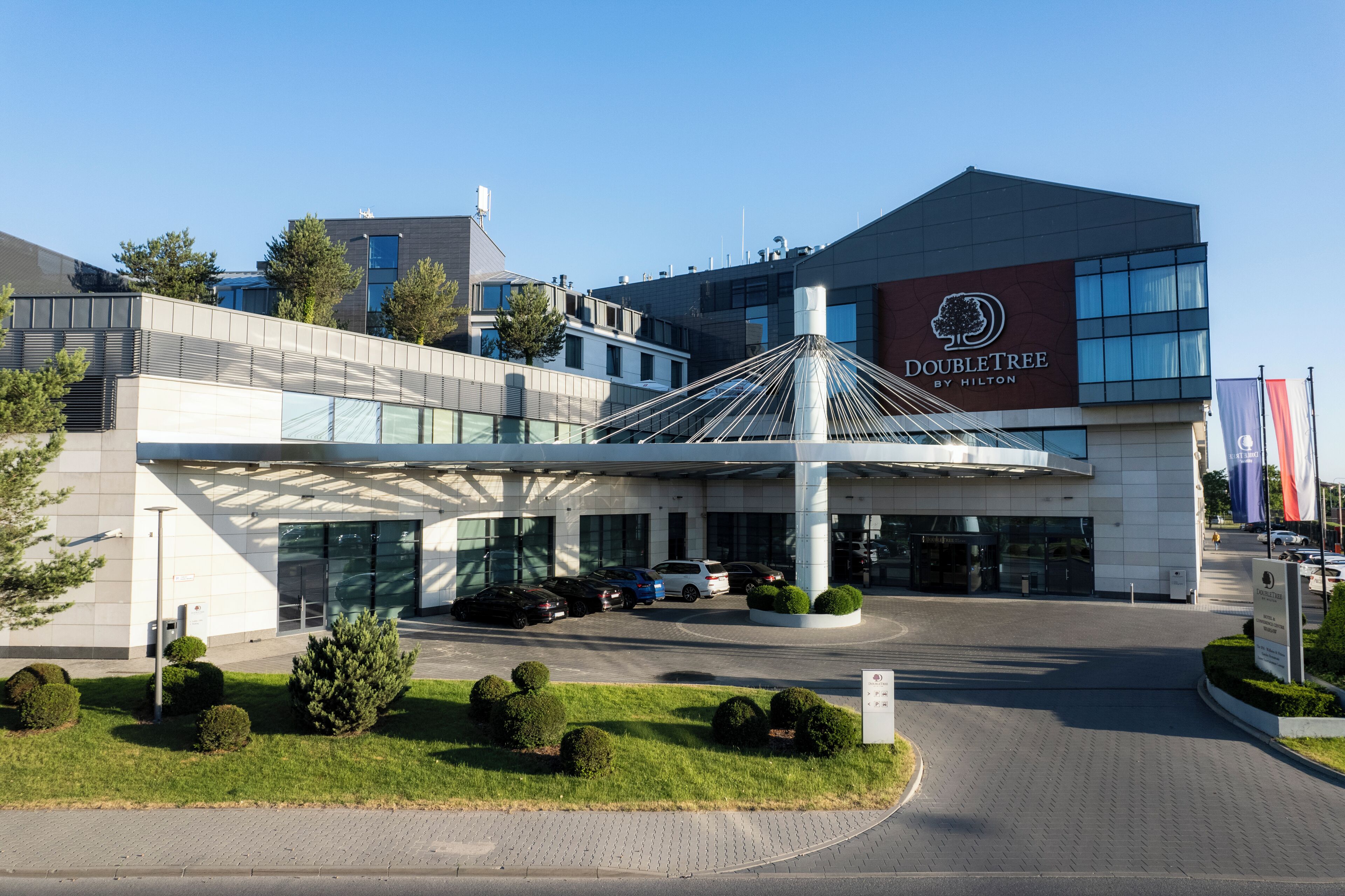 A modern hotel with a prominent DoubleTree by Hilton sign, a covered entrance, and a landscaped driveway.