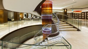 A modern hotel lobby with a central spiral staircase, glass railings, and a decorative light fixture. - DoubleTree By Hilton Hotel & Conference Centre Warsaw (Warsaw)