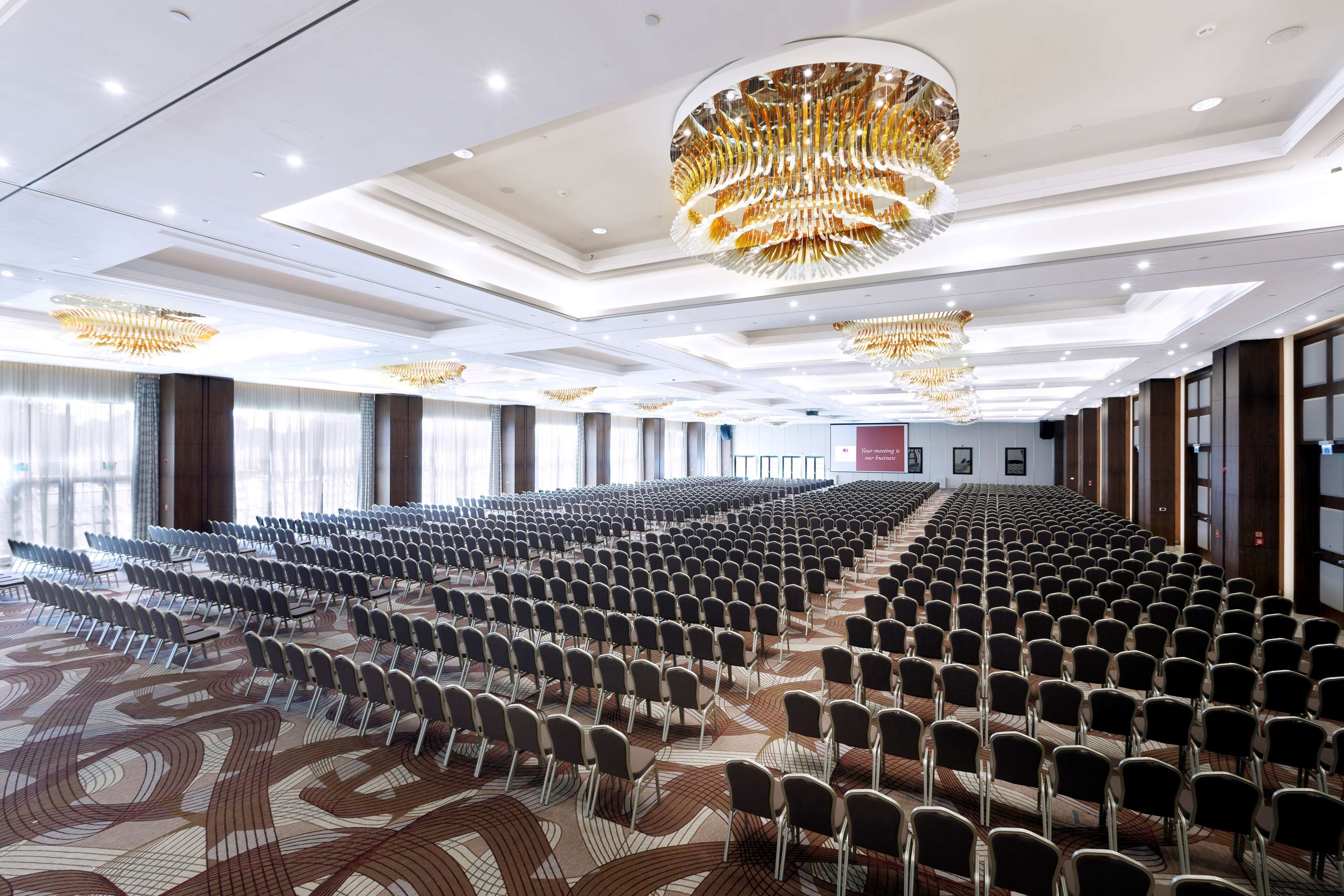 A large conference room with rows of chairs, a patterned carpet, and a modern chandelier.