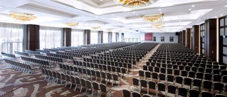 A large conference room with rows of chairs, a patterned carpet, and a modern chandelier.