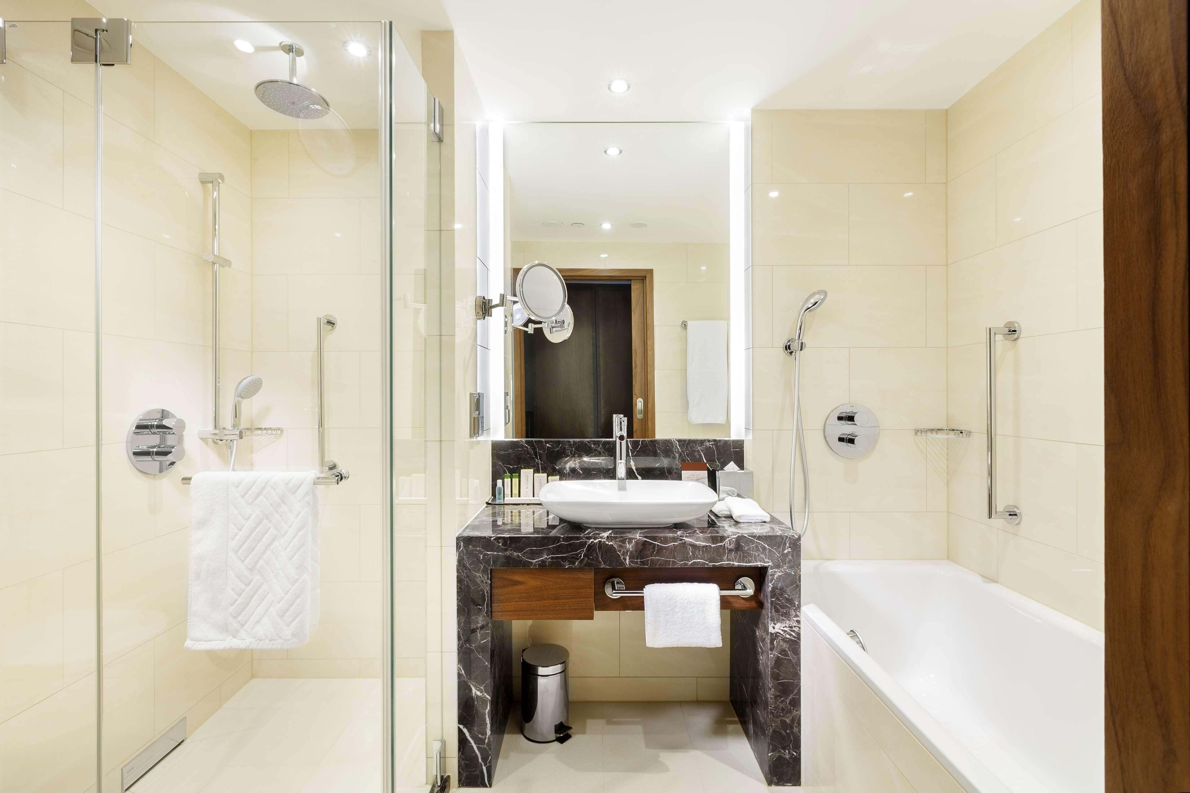 Un baño moderno con ducha envuelta en vidrio, lavamanos de mármol y bañera independiente.