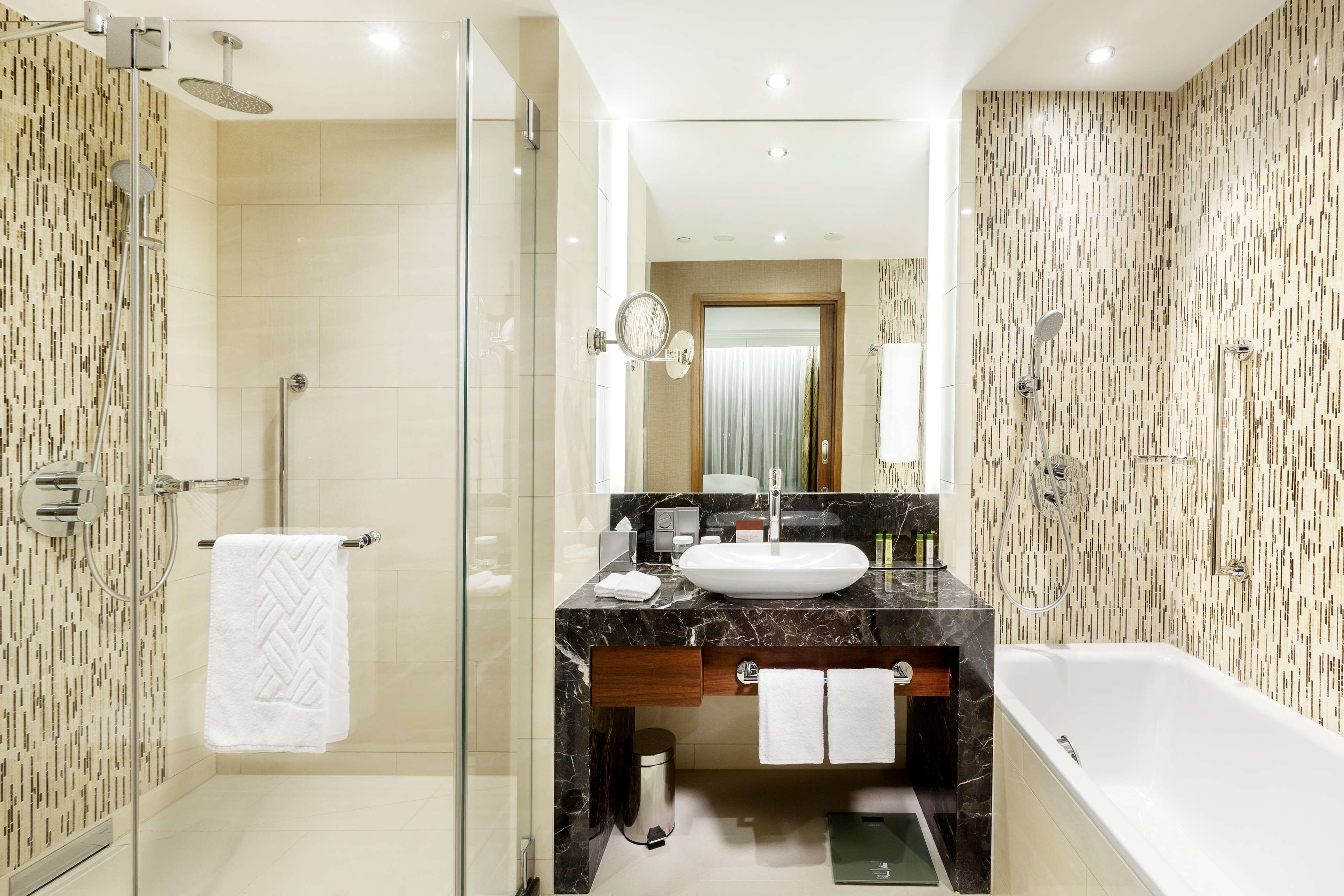 A modern bathroom with a glass-enclosed shower, a marble sink, and a bathtub.