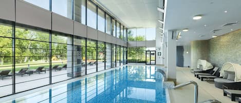 An indoor swimming pool with clear glass walls, a tiled floor, and a view of the outdoors.