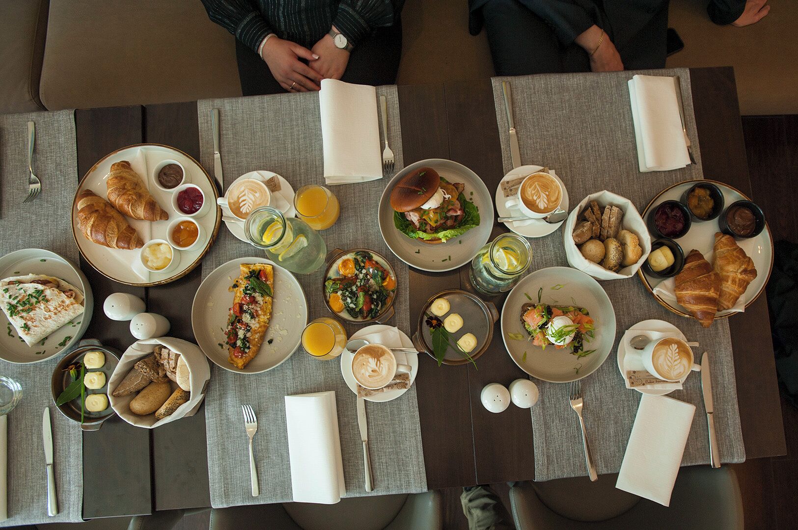 Una mesa de comedor con diversos productos para el desayuno, como cruasanes, tortillas y café.