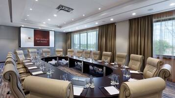 A conference room with a large oval table, beige leather chairs, water bottles, and a projector screen displaying a message.