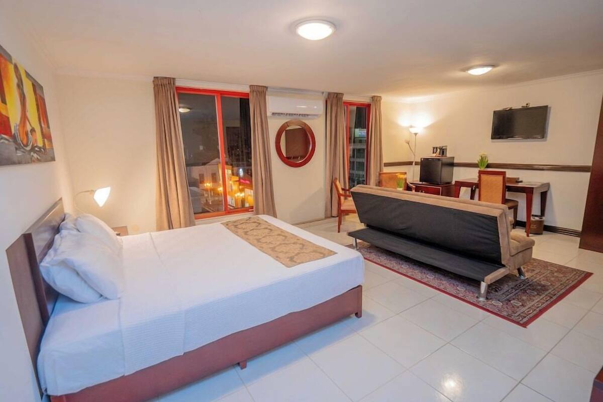 A hotel room with a bed, a sofa, a TV, and a desk.