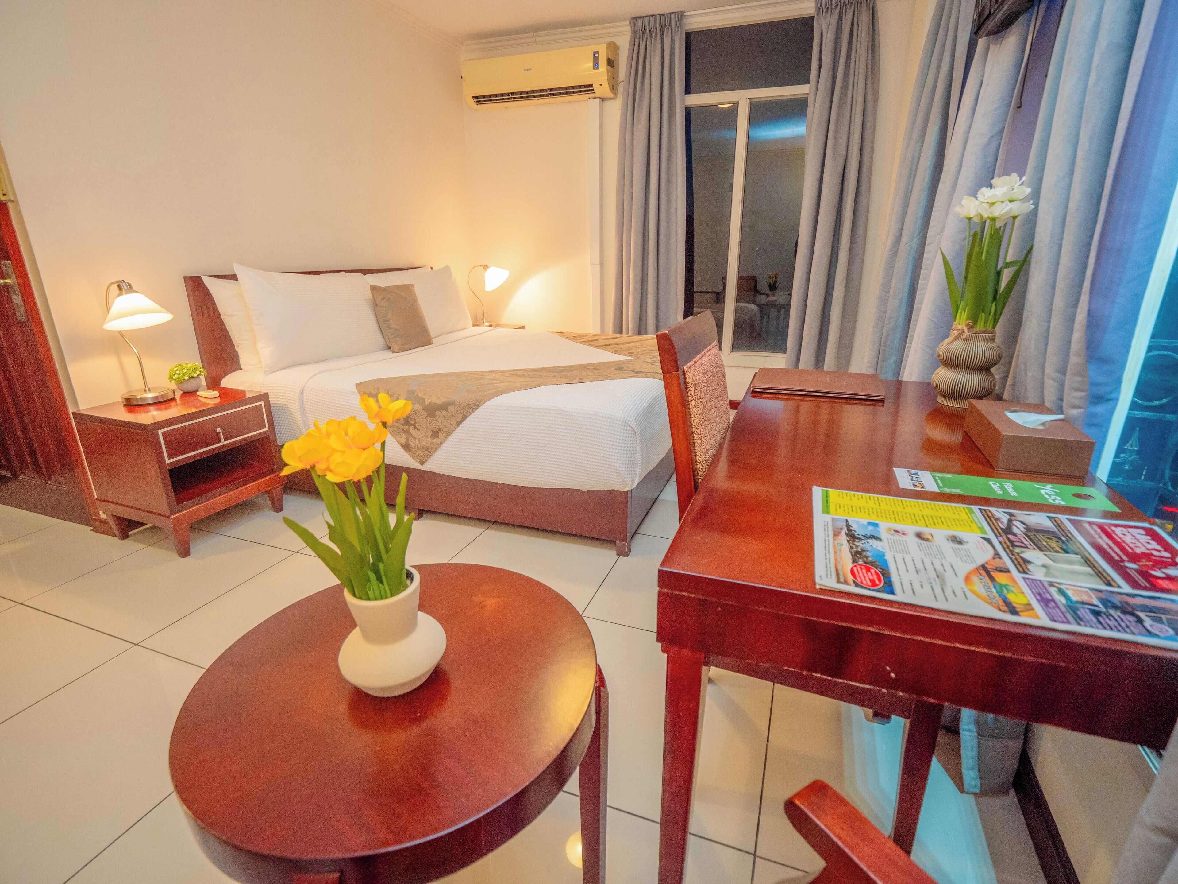 A hotel room with a bed, bedside tables, a round table, and a window with curtains.