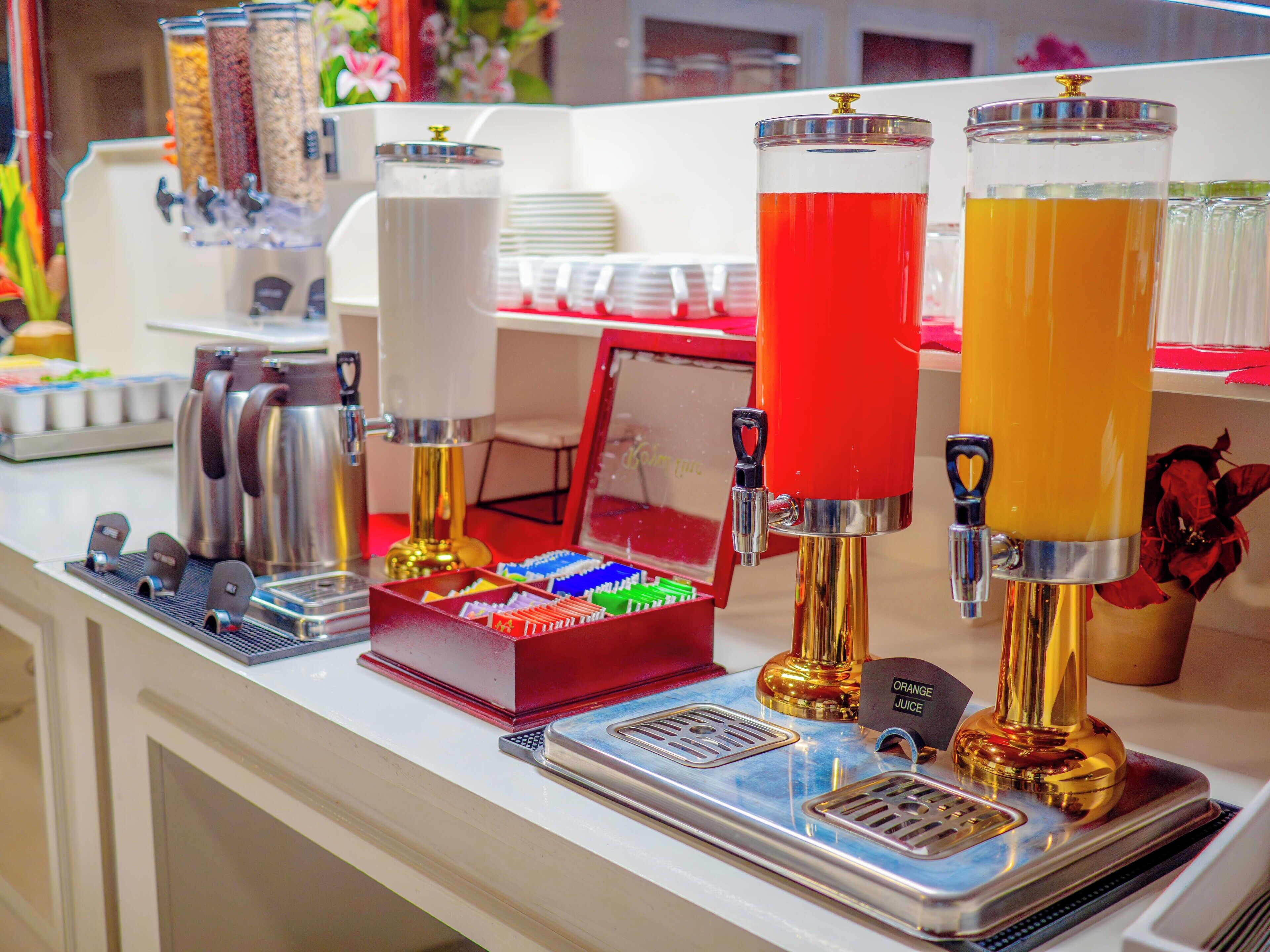 Estación de bebidas con varios dispensadores, una máquina de café y una bandeja con diversos artículos.