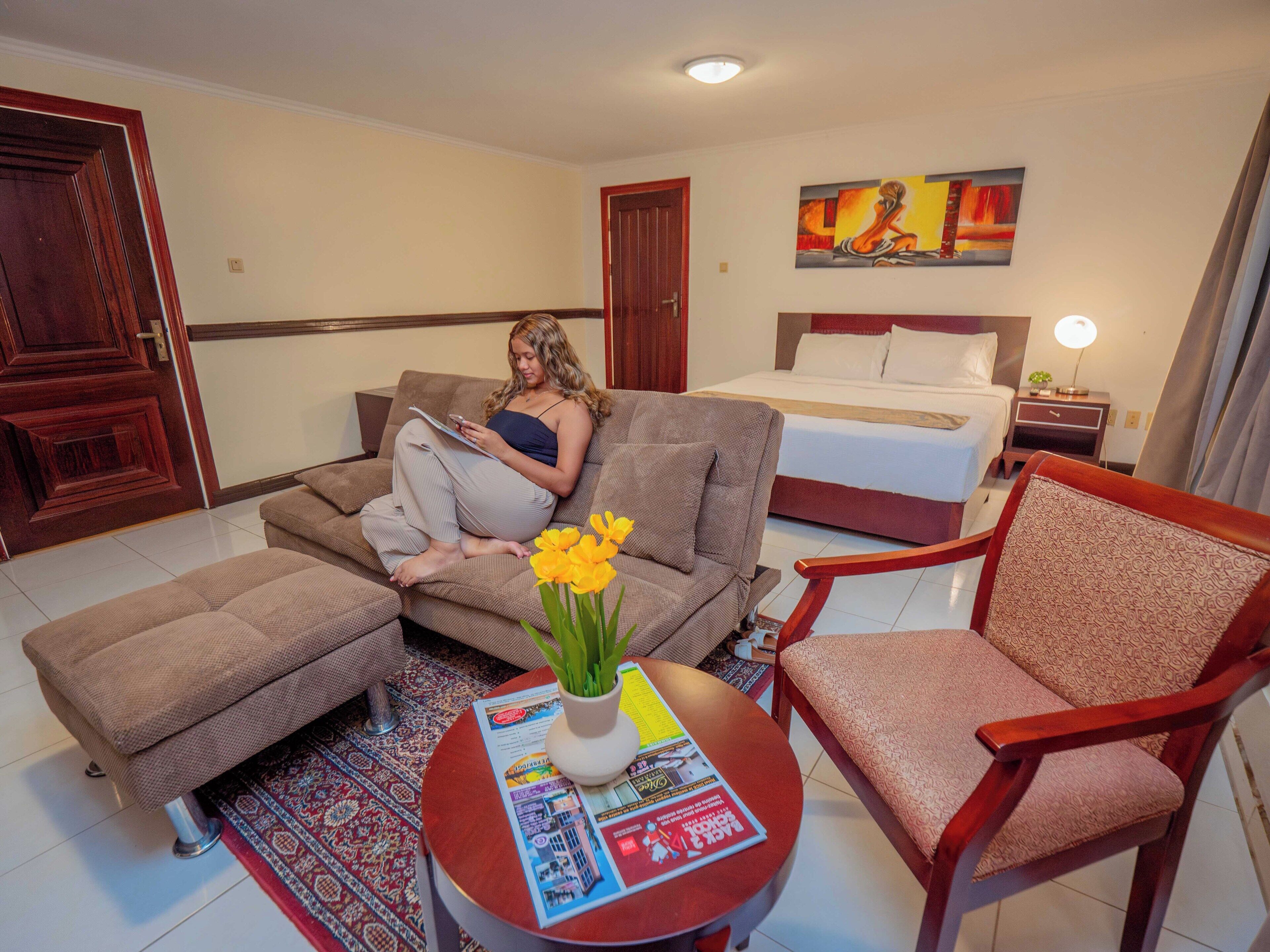Una habitación de hotel con una cama, un sofá, una silla, una mesita con un florero y un cuadro en la pared.