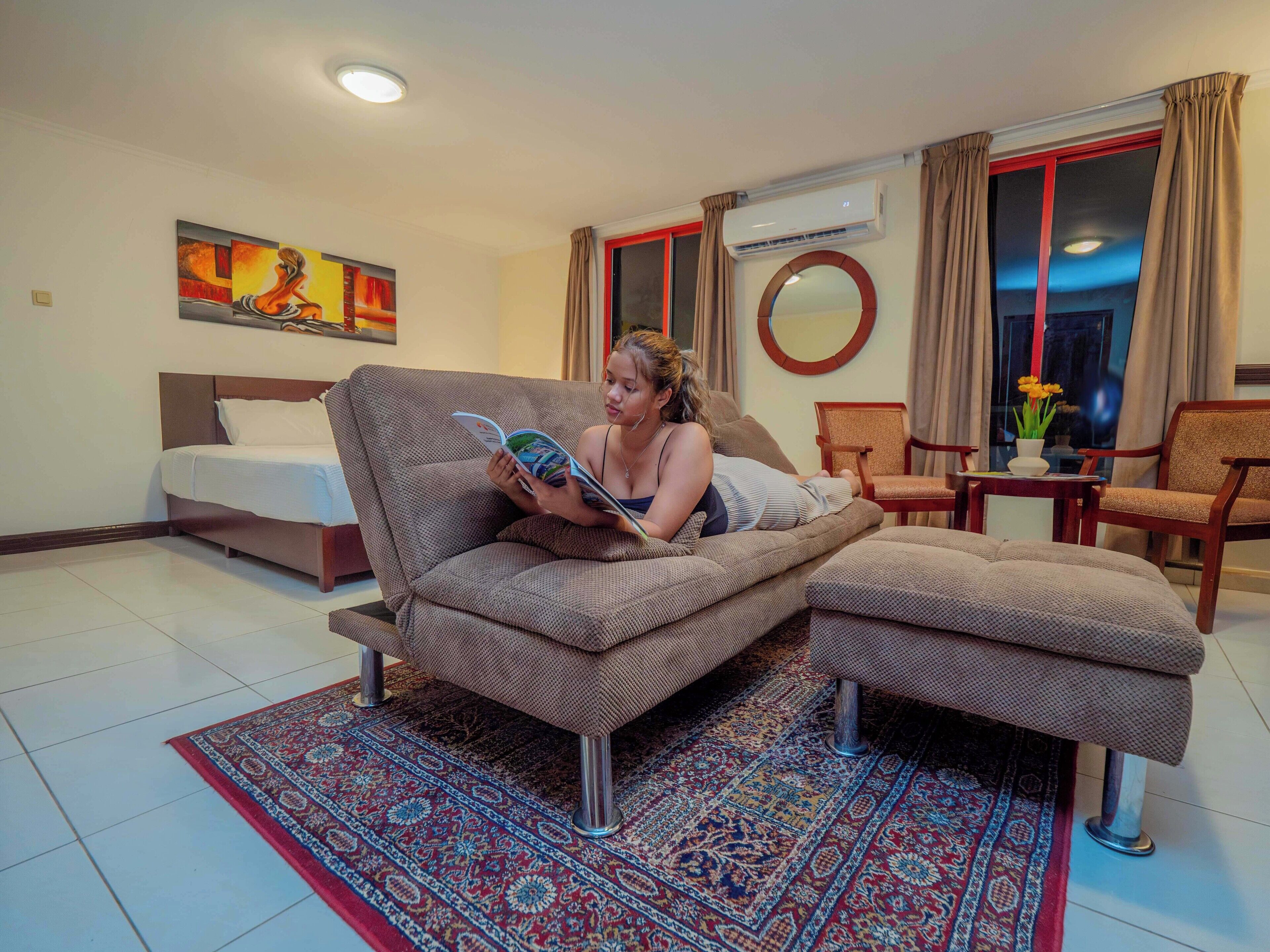 A modern living room with a sofa, a bed, a dining area, and a large window with curtains.