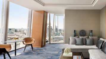 Une chambre d’hôtel moderne dotée d’une grande fenêtre donnant sur la ville, d’un ensemble de canapés, d’une table basse avec des livres et de deux fauteuils.
