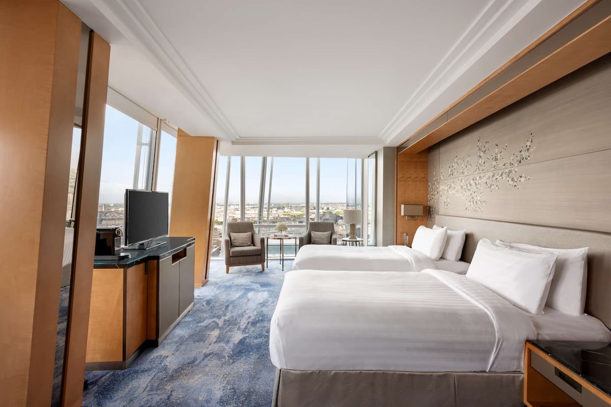 A hotel room with two beds, a desk with a TV, a small table, and chairs.