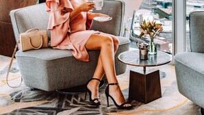 A woman sitting by a window with a city view, a small table with a vase, and a handbag on the armchair. - Shangri-La The Shard, London (London)
