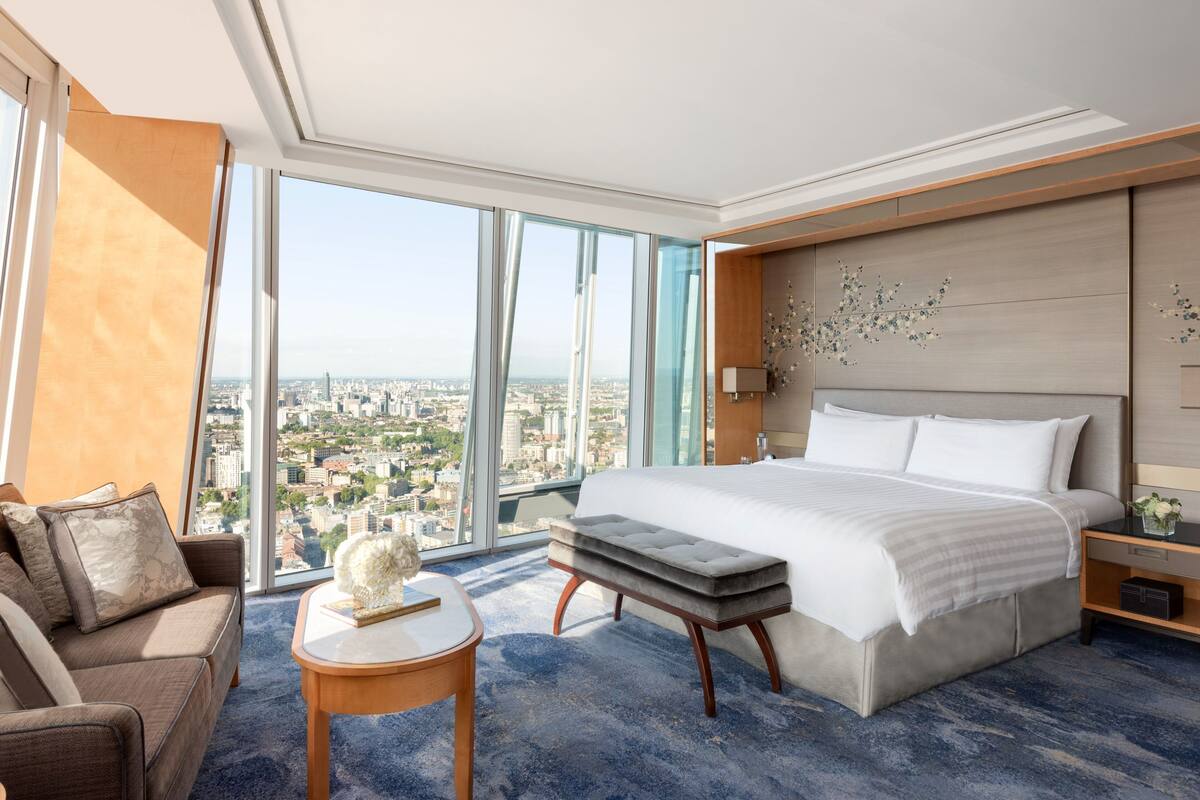 A modern hotel room with a large bed, a sofa, a small table, and a view of the city.