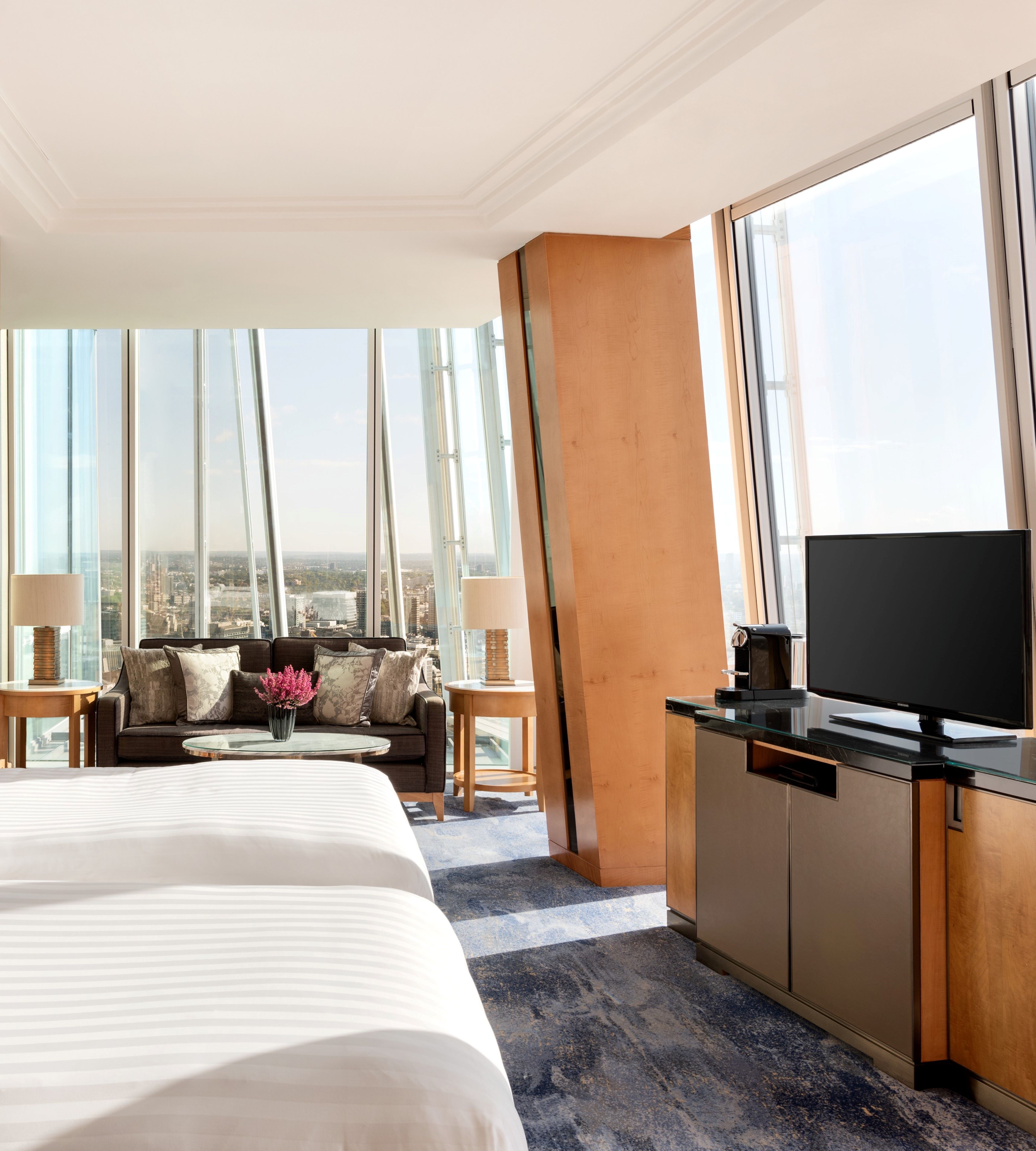 Ein Hotelzimmer mit einem großen Bett, einer Couch, einem Fernseher, einer Kaffeemaschine und Blick auf die Stadt.