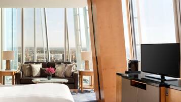 Ein Hotelzimmer mit einem großen Bett, einer Couch, einem Fernseher, einer Kaffeemaschine und Blick auf die Stadt.